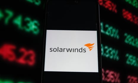 A Solarwinds logo is seen displayed on a smartphone with stock market percentages on the background. 