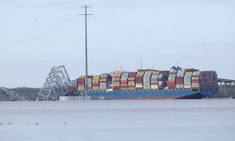 a giant blue ship with stacks of colorful shipping containers next to giant pieces of metal submerged in water
