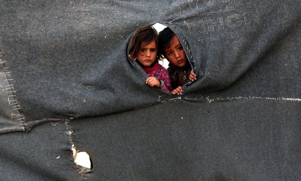 Two Syrian child refugees peer through a makeshift barrier at the Zaatari camp in Jordan.