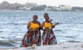Pendo and Leah Zawose on the Zawose Queens on a beach. Leah is holding an illimba thumb guitar.