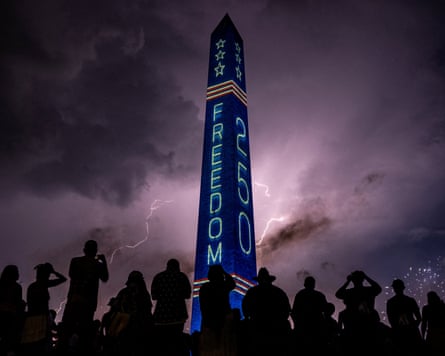 Lightning strikes behind the illuminated Washington Monument, as people gather to watch 250th anniversary fireworks.
