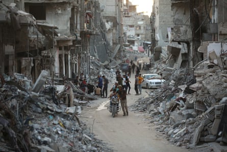 people walk between destroyed buildings