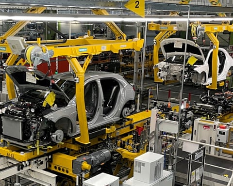 Car bodies hang from yellow overhead rigs on a Mercedes-Benz factory assembly line