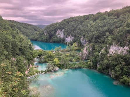 Wooded mountains along the banks of a bright blue river under purple cloudy skies