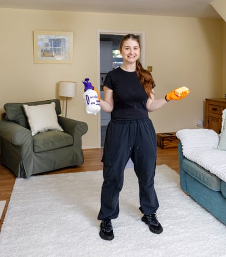 A woman in a black T-shirt and black trousers holding cleaning products in a clean room