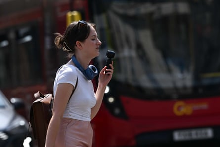 A woman holds a handheld fan to her face as she walks past a London bus