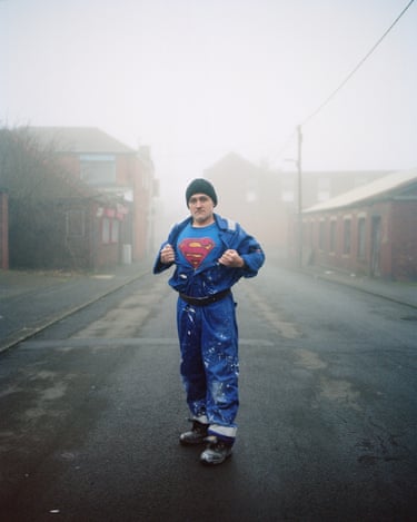 Andrei, man of steel (from the series Buried Treasure), 2024 Guardian photographer Ed Alcock follows his roots back to the mining village of Horden, County Durham, in order to ‘explore the tales of my maternal family … and the reality of a place that has become one of the poorest territories in Europe’. Andrei, a Romanian who recently settled in the village, stands in the mist and bears a Superman T-shirt beneath his paint-splattered overalls