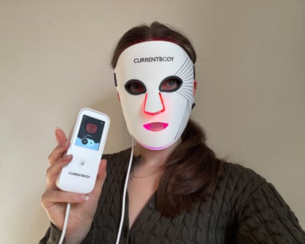 Sarah Matthews wears a white LED face mask glowing red and pink, holding its controller