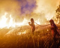 Two firefighters use a water hose to try to extinguish a spreading land fire