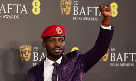 A young black man in a purple jacket and red beret gives a clenched-fist salute in front of a Bafta film award backdrop