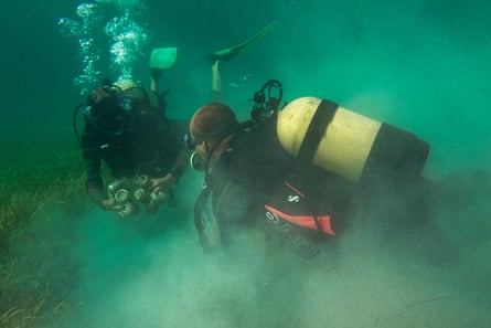 Two scuba divers clean up plastic and tins in murky water, Playa Larga, Cuba.