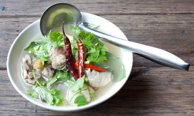 Duck soup: a shallow white bowl with green leaves and red chillies with a ladle on the edge