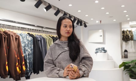 A young woman stands inside a bright modern-looking shop with rails of clothing.