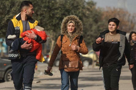 A member of the White Helmets carries a small child as a young man and woman follow close behind