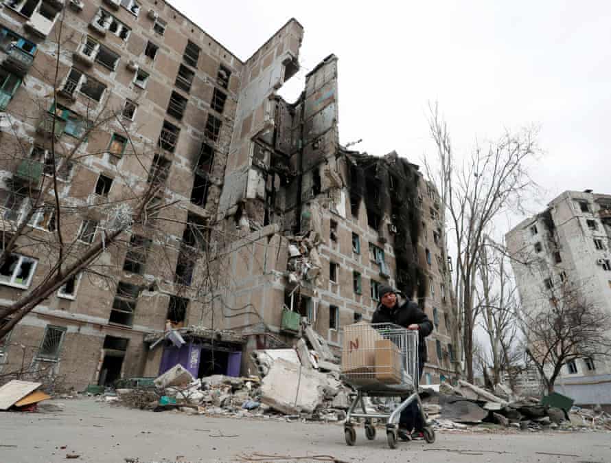 A local resident pushes a cart with humanitarian aid past a damaged apartment building in Mariupol.