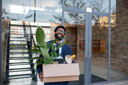 Happy businessman with carrying box with office supplies in front of glass wall