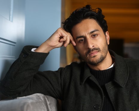 Imran Perretta wearing a black jumper and black wool jacket leans on his elbow and looks intently into the camera