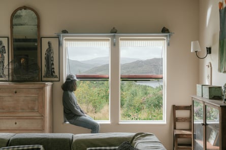 A young woman looks out of a window at a remote cottage