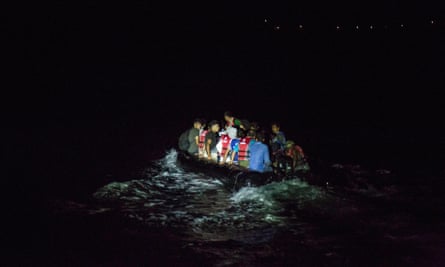 Shot of an overcrowded rubber dinghy at sea in darkness, picked out by a searchlight
