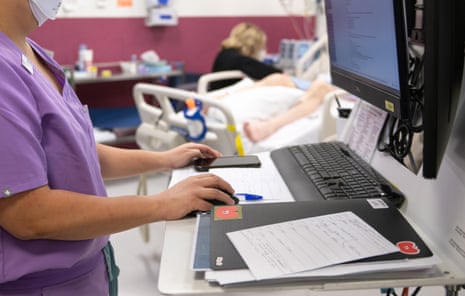 Hospital staff at a desk check paperwork in front of a computer