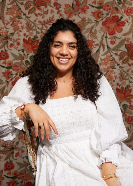 Dina Macki wears a white dress and is sitting, smiling, in front of a floral backdrop