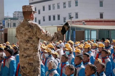 A man in army fatigues stands in front of rows of children in uniform.