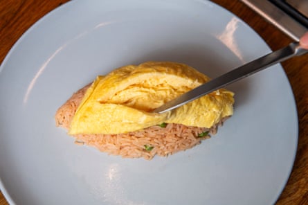 A knife cuts open a soft omelette on a mound of rice.