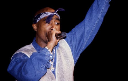 The rapper on stage wearing a blue shirt and white vest with a bandana tied around his head