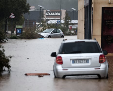 Cars are partly submerged in floodwater on a street near shops in France