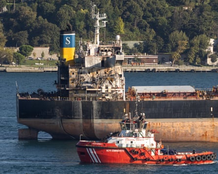 A damaged Liberian-flagged bulk carrier is escorted by a red safety boat