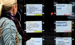 A woman passes notices for jobs in the window of a recruitment agency in London