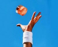 A hand with a wristband reaches up into a blue sky to catch a jar of face cream.