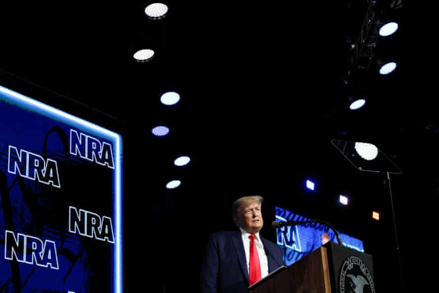 Donald Trump speaks on stage in front of NRA branded backdrops.