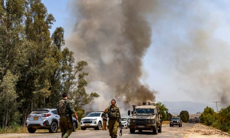 Israeli soldiers on a highway, with a plume of smoke rising in the distance