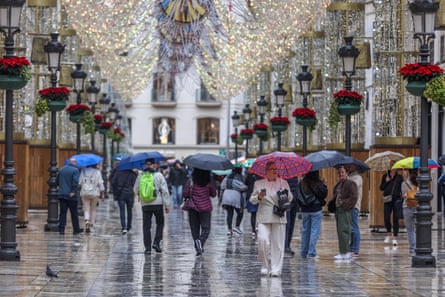People walk through a pedestrianised road holding umbrellas in the rain in Málaga, Spain.