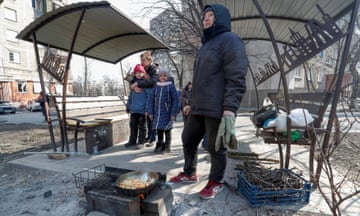 People prepare food in an icy urban yard beside covered park benches