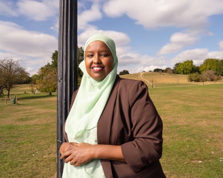 A woman wearing a hijab, Labour election Sagal Abdi-Wali, smiles as she leans against a lamp-post in a park.