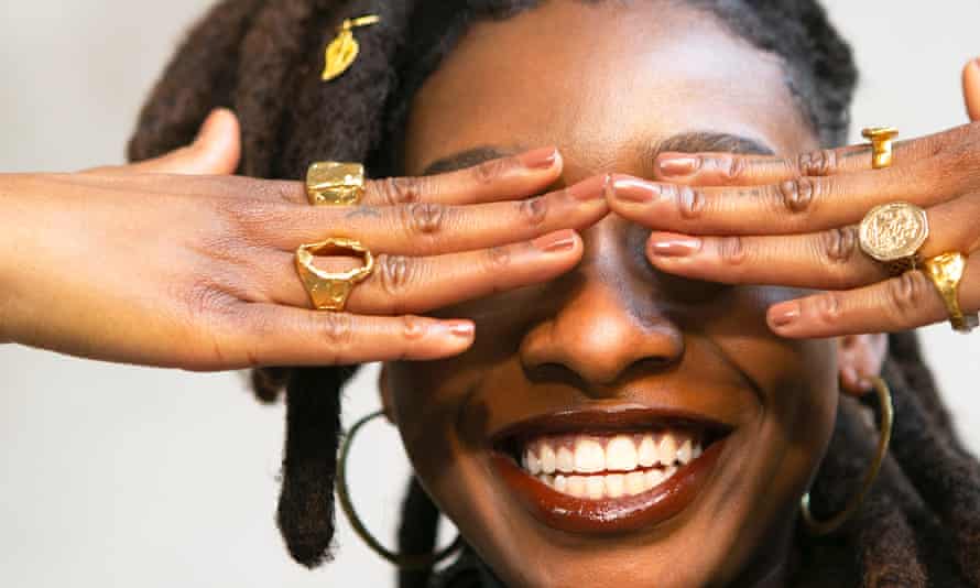 Little Simz with big gold rings and fingers over her eyes, smiling