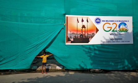 A boy pulls up plastic sheeting placed to screen a slum area alongside a road before the G20 summit in Delhi