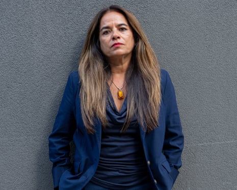 Pia Sinha poses in a navy suit against a dark grey wall.