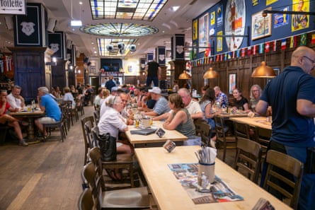A long beer hall with colourful poster and flags, and a stained-glass ceiling