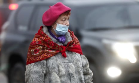 A Russian woman walks on a street in the town of Podolsk, outside Moscow, on 27 November. She wears a beret, red scarf and blue face mask.