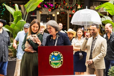 A woman standing behind a lectern. Another woman standing next to her is holding a pig in he hands.