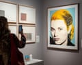 A woman in shadow holds her cellphone up to a lighted image of Grace Kelly.