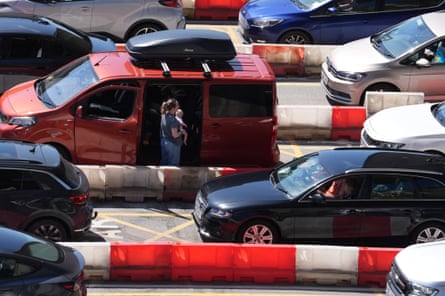 A woman and her baby standing outside their campervan in a queue of traffic