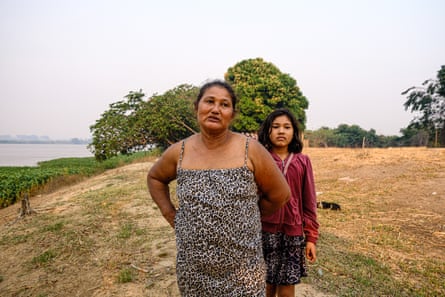 A woman and her daughter standing on a grassy hill with green tree behind them. 