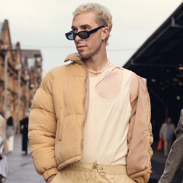 A man wearing cream-coloured clothes and black sunglasses walks down a street