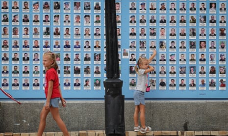 Girls play next to the memory wall of fallen defenders of the country in Kyiv
