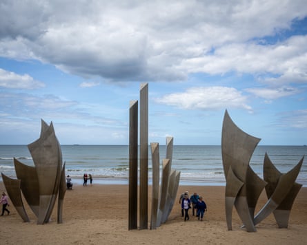 People looking at a large abstract sculpture on a beach