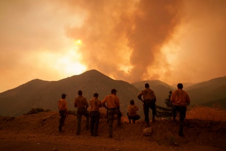 grow of people stand with backs turned to look at mountain with smoke rising above